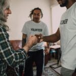 Uśmiechnięci wolontariusze zbijają piątkę w sali podczas spotkania