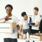 Wolontariusze w różnym wieku sortują ubrania i dary przy kartonach