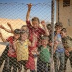 Dzieci uchodźców stojące za ogrodzeniem obozu w Idlib w Syrii