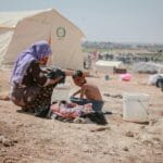 Syryjska uchodźczyni pierze ubrania z dzieckiem w obozie